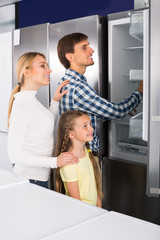 Smiling couple with girl choosing refrigerator