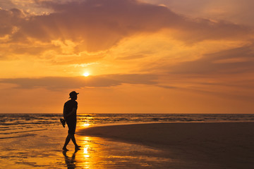 Fototapeta na wymiar Man walking along the beach at sunset