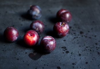 Several ripe juicy homegrown plums lying on a black table. Morning in the village, the time of harvest. Plums are dark purple, sweet, tasty and full of juice. Water splashed around.