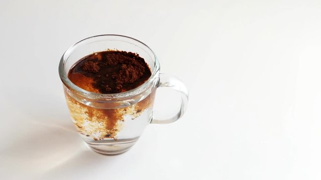 Making instant coffee in transparent glass.Putting instant coffee extract into mug. Stirring coffee. Coffee steaming.