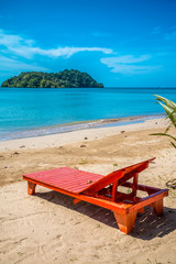 Obraz na płótnie Canvas Red daybed on beautiful tropical island beach in sunny day blue sky background. Summer tropical travel holiday vacation or green nature concept.