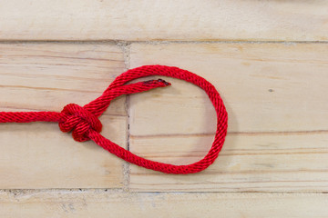 Obraz premium bowline knot made from red synthetic rope, tightening on wooden background