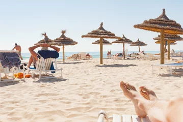 Fotobehang Strand houten stro zonnescherm paraplu benen mensen zonnebaden ontspannen Tunesië © matousekfoto