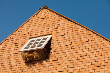 Brick made farmhouse with window open and truss straw inside against blue sky background.