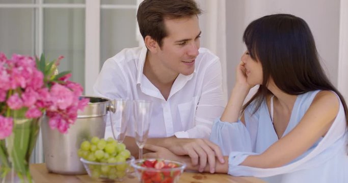 Attractive mixed couple having wine and fruit together at table with pink flower bouquet