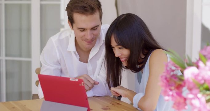Happy young adult man and woman showing off ultrasound pictures of baby in womb to someone through a video chat on their tablet computer