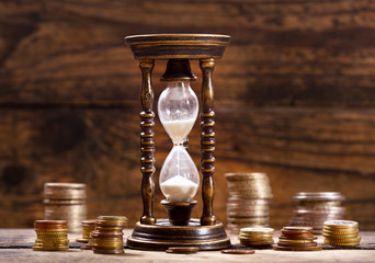 hourglass and coins on wooden background