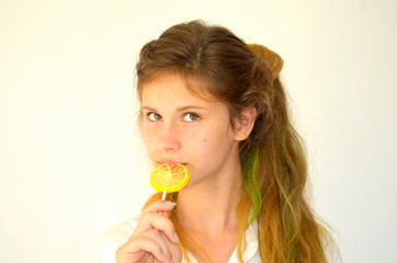 Obraz na płótnie Canvas Молодая девушка с разноцветными волосами в белой рубашке на белом фоне с леденцом в руках в виде лимона 
