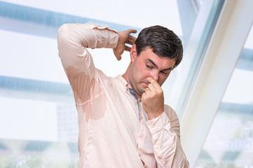 Man with sweating under armpit pinches nose with fingers