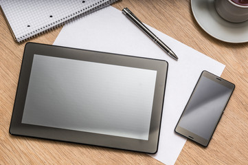 Tablet, mobile phone, pen, note and cup of coffee on table