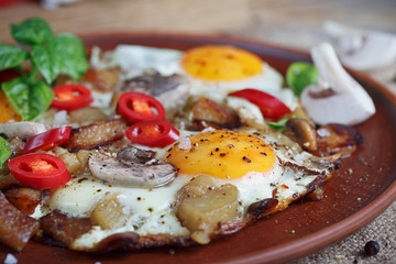 Fried eggs with mushrooms, tomatoes and basil on rustic wooden t
