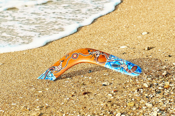 Colorful boomerang on sandy beach near sea surf.