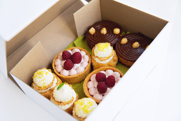 Desserts in the white paper delivery box. Freshly baked tarts and eclairs in the box. Desserts package. - 118757915