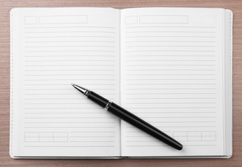 Open notepad and pen on wooden background