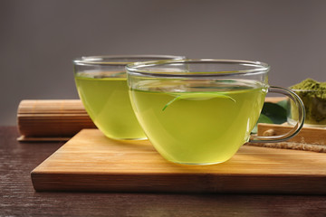 Glass cups of green matcha tea on wooden cutting board closeup