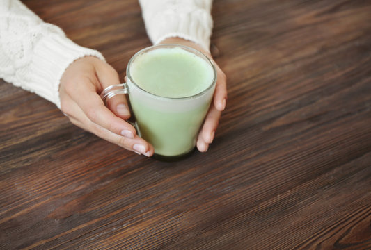 Female hands holding cup of green matcha tea on wooden background