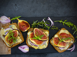 Baked toasted of dark bread with blue cheese and figs served on cutting board.