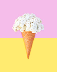Ice cream cone with flowers over pink yellow background top view