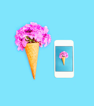 Ice cream cone with flowers and smartphone over blue colorful ba