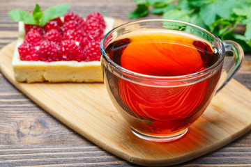 Raspberry cake with a cup of tea on the wooden background with mint leaves