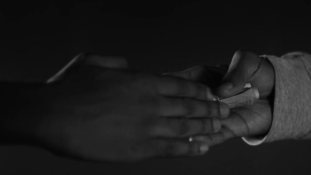 Black and white shot of hands exchanging money for drugs, in slow motion