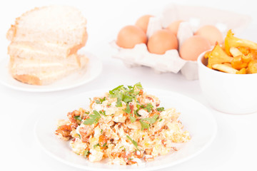 Scrambled eggs with chanterelle and parsley with some white bread on a white background