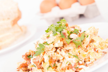 Scrambled eggs with chanterelle and parsley with some white bread on a white background