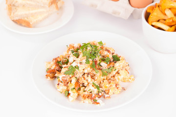 Scrambled eggs with chanterelle and parsley with some white bread on a white background © teine