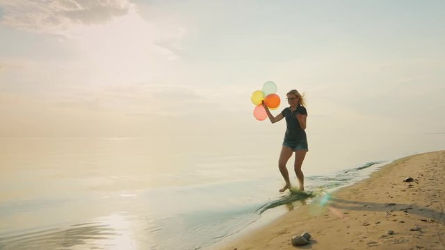 Carefree young woman running on the beach, holding balloons in his hand. Concept - the ease, freedom, joy,