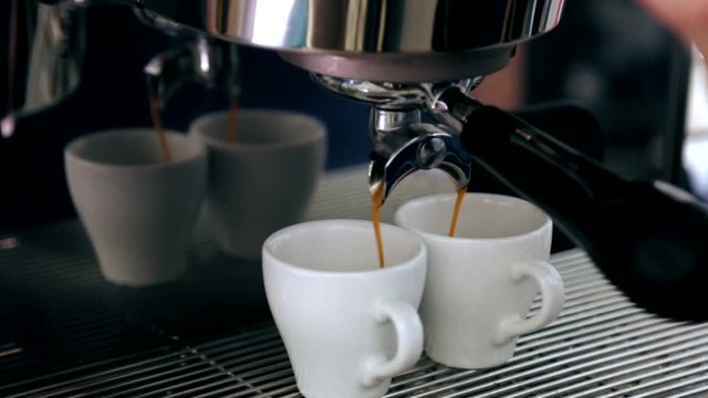 The cappuccino is poured into two mugs from the coffee machine