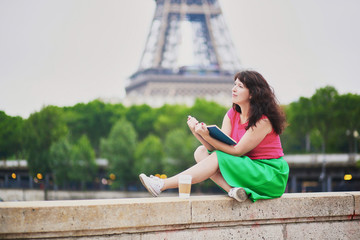 Girl with coffee to go reading a book near the Eiffel tower.