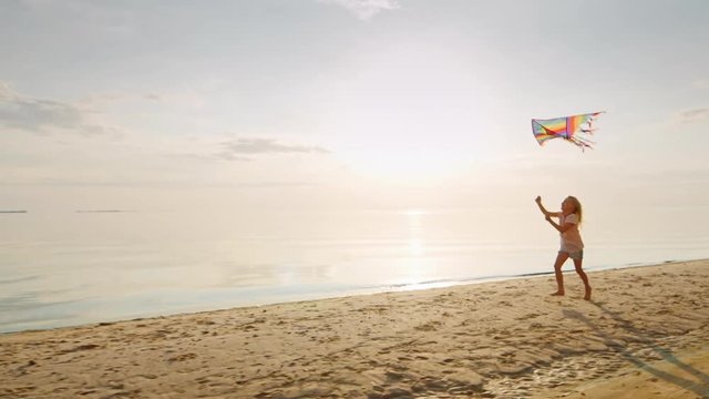 Happy little blond girl is running with a kite. On the seashore at sunset. Concept - childhood dreams and a happy childhood