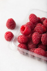 fresh, organic raspberries in a plastic container over white background, selective focus, close up, studio, vertical