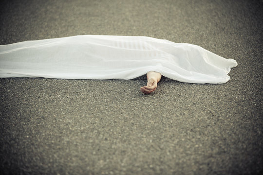 Dead body covered with sheet and hand sticking out