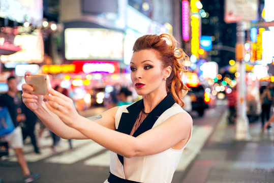Beautiful tourist woman fashion blogger taking photo selfie on night Time Square in New York City