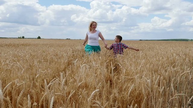 Mother and son running on the wheat field. Happy family in summer field