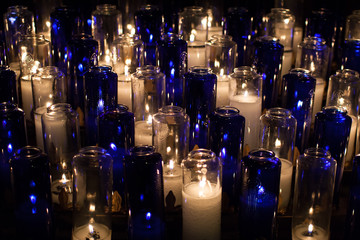 close up of burning candles in blue and white transparent chandeliers in a church