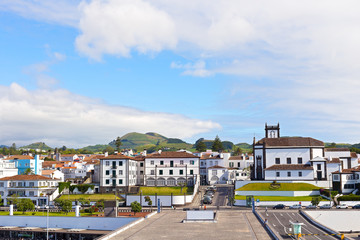 View on Ponta Delgada from the ocean pier, Azores, Portugal. White houses with colorful tiled roofs and countryside with mountain ridge on the horizon.