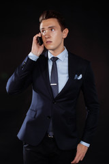 young pretty business man standing on black background, modern hairstyle, talking on phone emotional