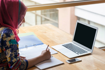 Muslim woman working with computer in the room , writing paper.