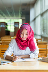 Beautiful young asian muslim woman working with files and laptop.