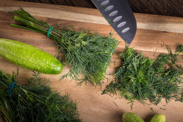 Sliced twig of dill on a wooden board with cucumber and knife