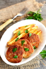 Fried meat cutlets served with fried potatoes. Turkey fillet cutlets with potatoes on the plate. Fork, sprig of fresh parsley on an old wooden background. Lunch or dinner menu. Closeup