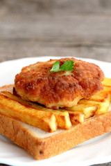 Sandwich with fried potatoes and Turkey meat cutlet on a plate and on old wooden table. A sandwich cooked from white bread, fried potatoes and Turkey burger. Closeup 