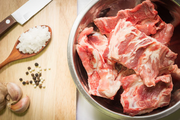 Raw pork ribs in stainless steel bowl with ingredients on a cutting board 