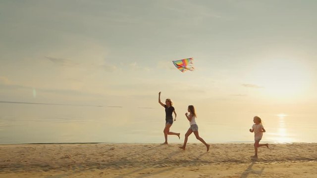 Mother with two daughters playing on the beach with a kite. The fun run together. Happy childhood
