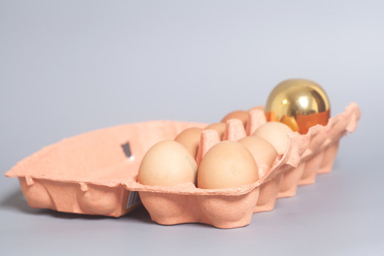 Cardboard egg box with golden and chicken eggs on gray backgroun