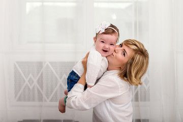 Mom kisses her little daughter on the cheek. Mom and daughter dressed in white shirts and jeans