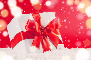white decorative christmas gift box with ribbon on snow against red festive background