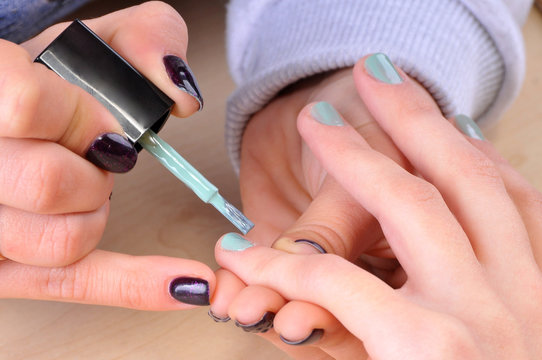 Nail salon - Applying green nail polish on female fingers.